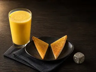 Mango lassi with two cardamom toast triangles arranged in a V beside the glass