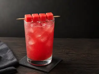 Limonada de sandía color rubí con cuatro cubos de sandía acomodados como una barra segmentada sobre el vaso