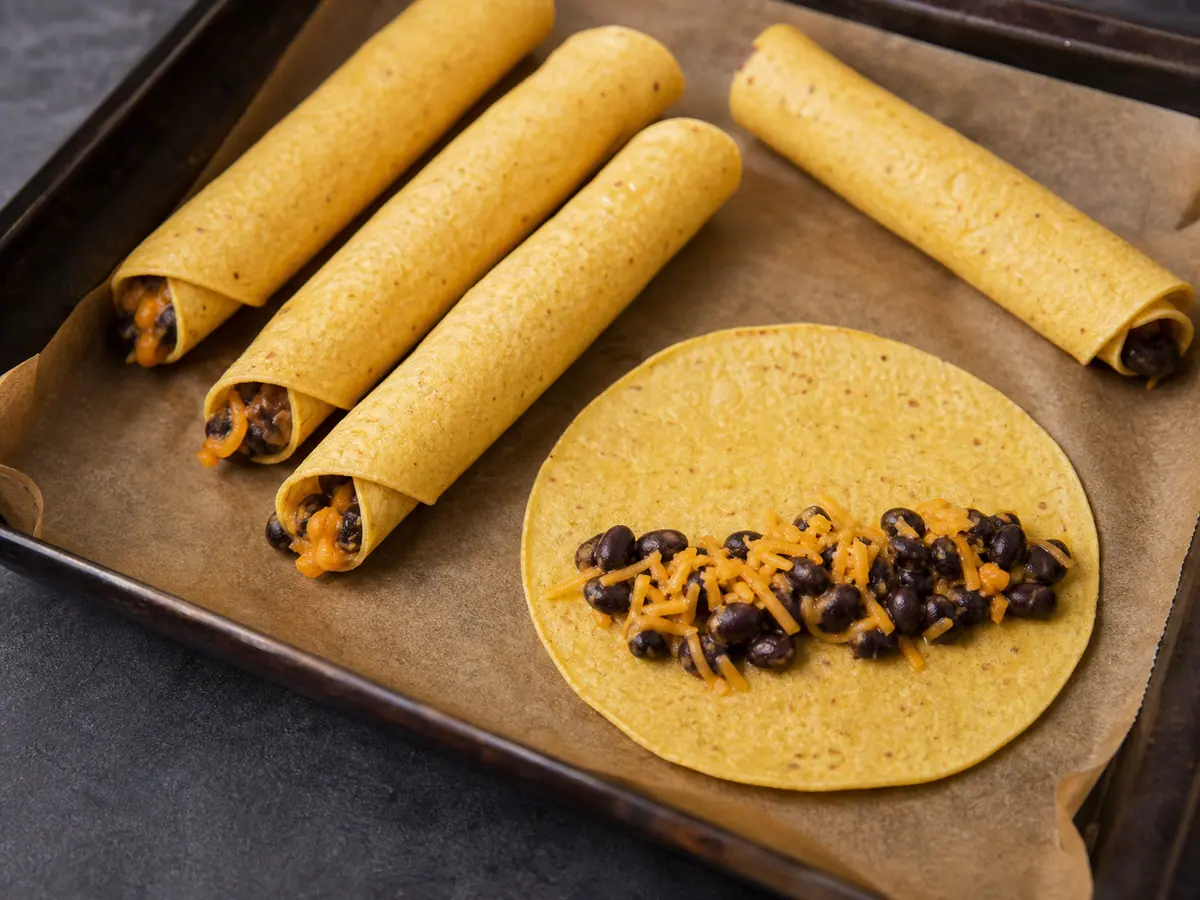 Eight pale unbaked taquitos from one of two sheets resting seam-side down on parchment