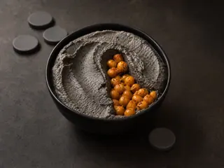 Pasta de gergelim preto, escura como carvão, com um sulco de colher que revela o crocante dourado de bolacha de arroz, servida com palitos de pepino e bolachas de arroz integral
