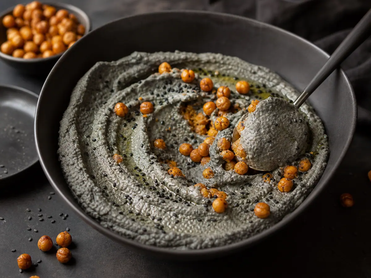 Pasta de tofu com gergelim preto parcialmente espalhada sobre pedaços grossos de bolacha de arroz em uma tigela rasa
