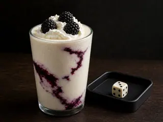 Milk-shake claro de baunilha com faixas de amora em roxo-escuro ao lado de um único dado mostrando um resultado baixo