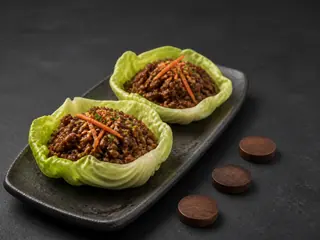 Two bulgogi cabbage cups with carrot, scallions, and sesame seeds on a dark platter