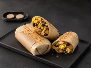 Dois burritos de café da manhã crocantes, um cortado ao meio e apoiado no outro, ao lado de duas fichas sem marcações sobre a mesa