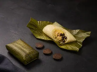 Two banana-leaf coconut rice parcels, one opened to show banana and black beans