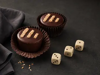 Dos vasitos de chocolate oscuro y coco con líneas descendentes de coco tostado, junto a tres dados que marcan la cuenta regresiva
