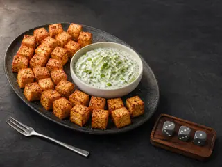Golden crispy tofu cubes arranged around cucumber-mint yogurt dip