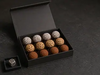 Caixa escura aberta com trufas de chocolate amargo cobertas com cacau, avelã e coco