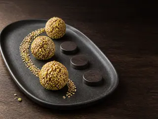 Three date tahini bites coated with pistachios and sesame on a dark game-night plate