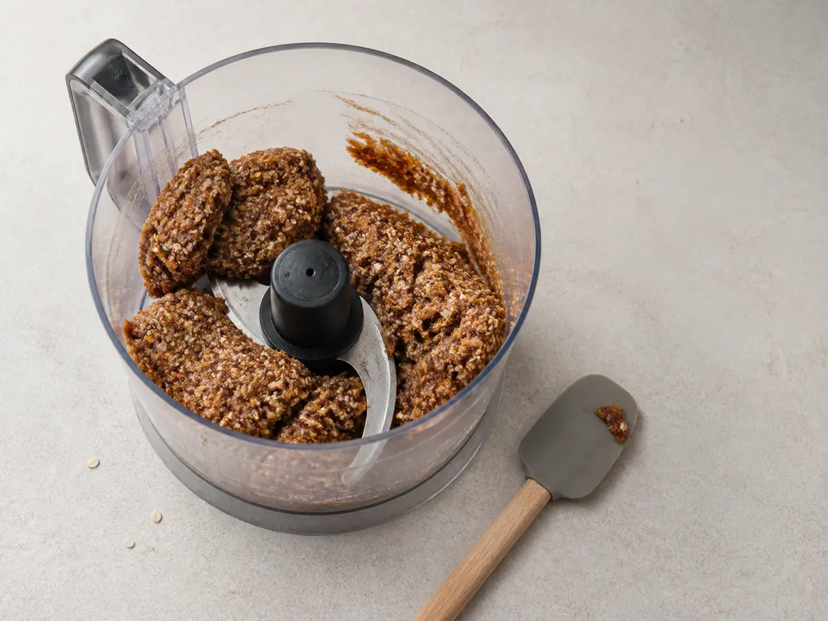 Cohesive date tahini oat mixture gathered in soft clumps in a food processor bowl