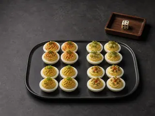 Sixteen deviled egg halves in four topping groups beside a single six-sided die