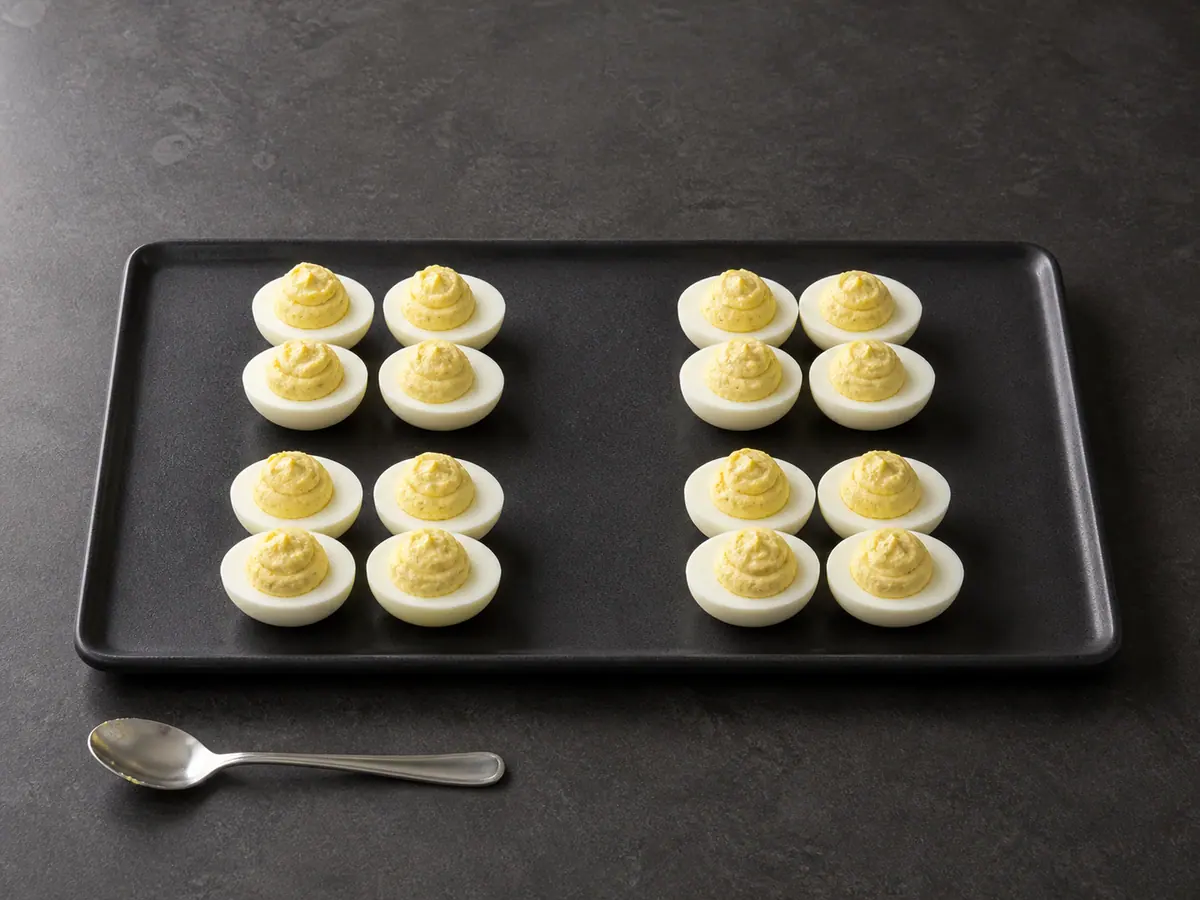 Sixteen egg-white halves filled with compact yolk mounds in four separated groups
