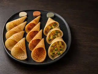 Three groups of crisp dosa cones on a dark platter: plain, podi-brushed, and potato-pea filled
