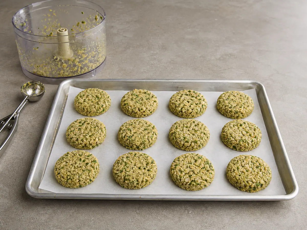 Twelve uncooked falafel patties shaped into rough-edged rounds on parchment