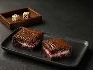 Two fudgy chocolate brownie squares revealing raspberry cream cheese centers beside neutral dice