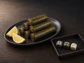 Stepped stack of six vegetarian stuffed grape leaves with lemon and a neutral dice tray