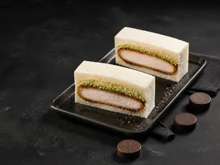 Dos mitades de un katsu sando de cerdo que muestran las capas de chuleta crujiente, col y salsa