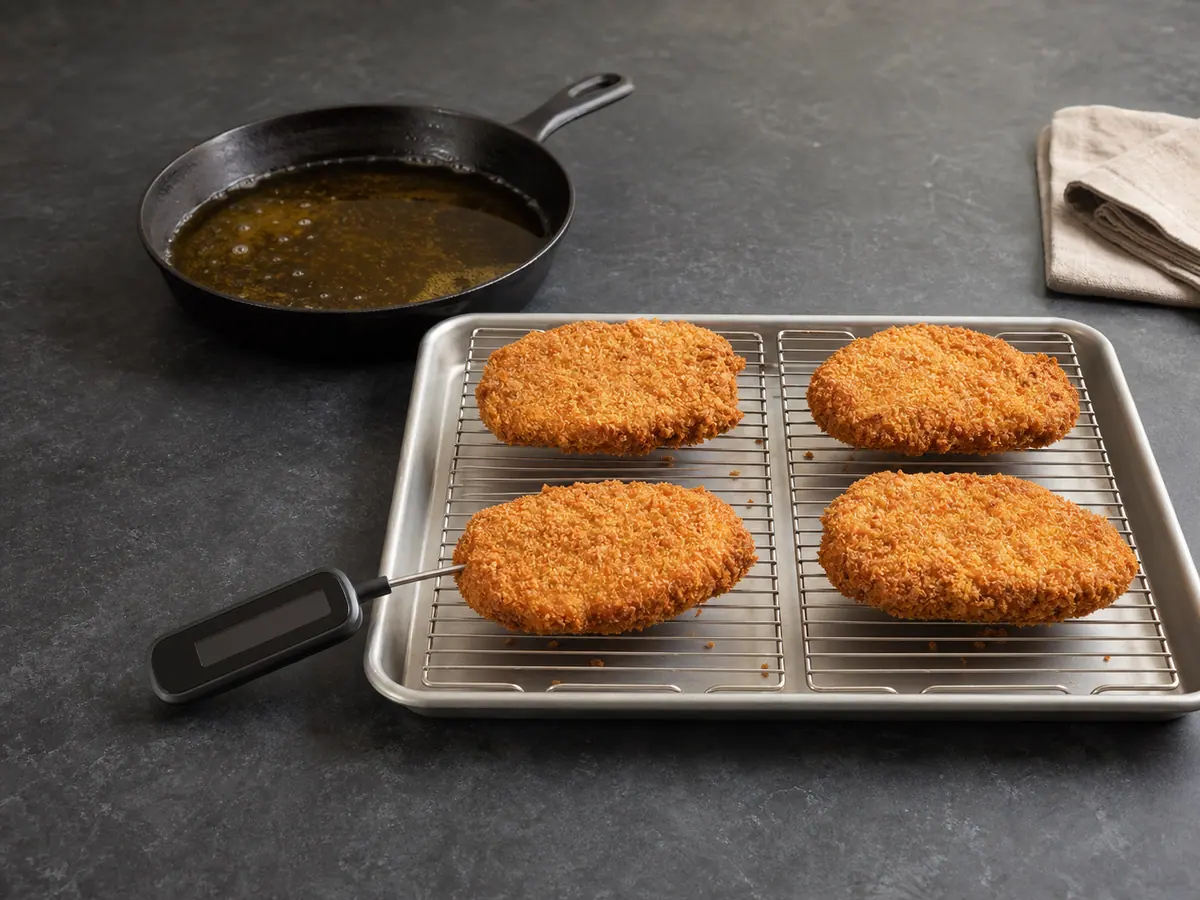 Four golden cooked pork cutlets draining on a clean rack with a thermometer probe in the front cutlet