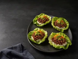 Four sweet-spicy Korean-inspired beef lettuce cups with rice, cucumber, carrot, scallions, and sesame