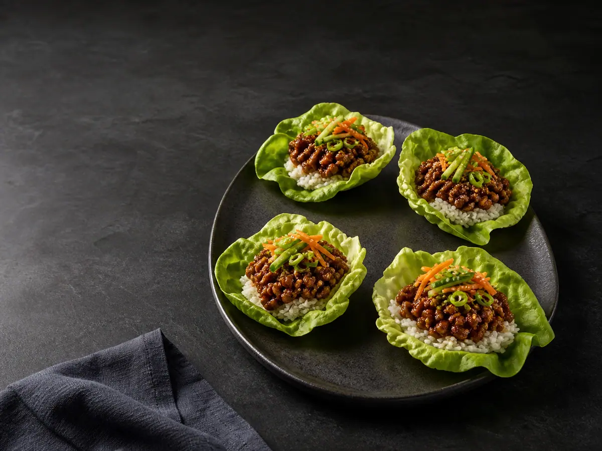 Cuatro hojas de lechuga rellenas con carne de inspiración coreana dulce y picante, arroz, pepino, zanahoria, cebollín y sésamo