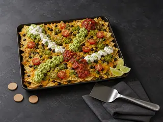 Layered nacho board with branching salsa, avocado, and jalapeño topping trails