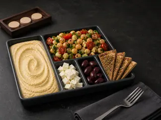 Bento de mezze de cinco compartimentos con hummus, ensalada de garbanzos, queso feta, aceitunas y triángulos de pan pita con za'atar