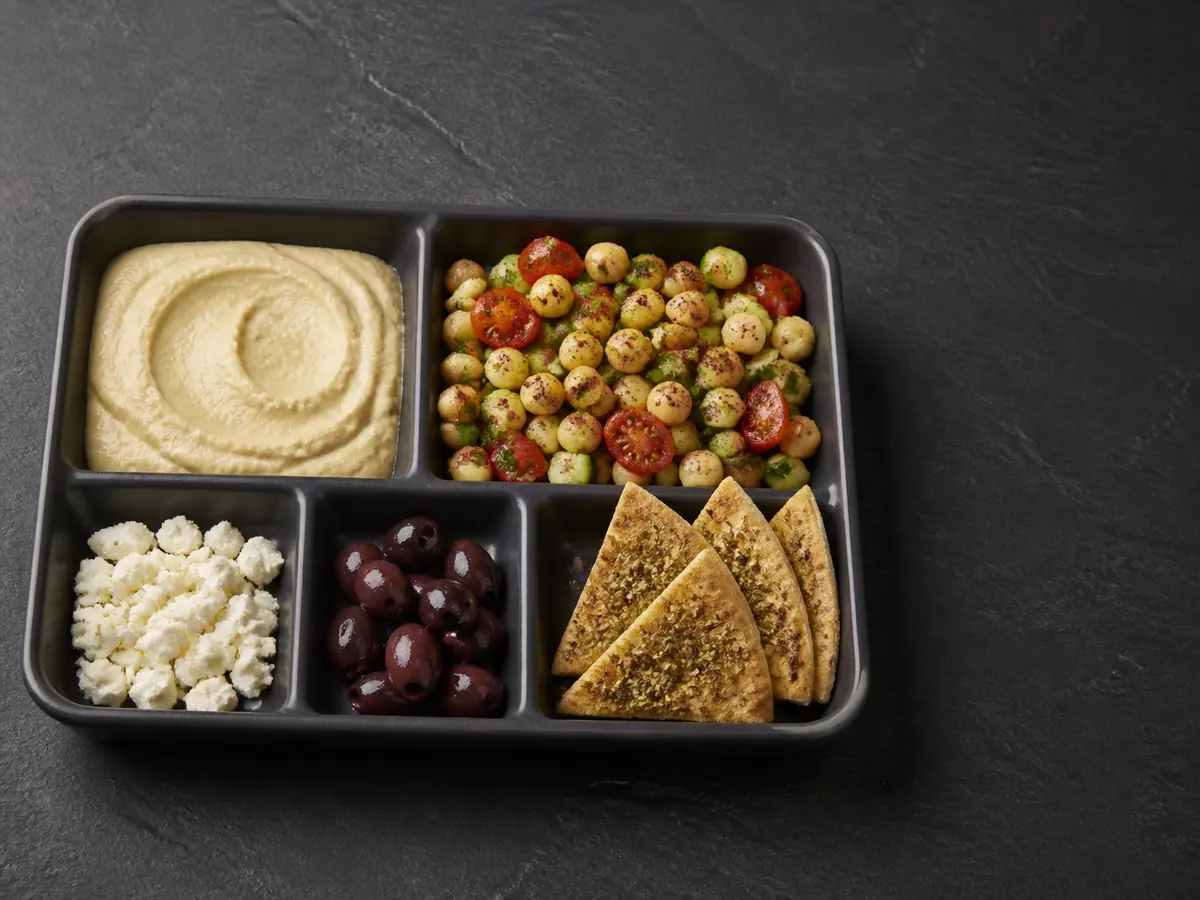 Five-compartment mezze tray with hummus, chickpea salad, feta, olives, and pita kept in separate slots
