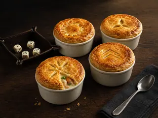 Four golden mini chicken pot pies with distinct pastry vent patterns arranged beside a neutral dice tray