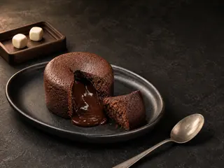 Bolinho de chocolate aberto, com centro de ganache derretida, ao lado de dois dados sem marcação