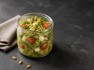 Open jar of shaken pesto orzo salad with chickpeas, tomatoes, mozzarella, arugula, and toasted pine nuts