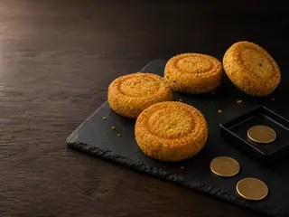 Four round potato croquettes with shallow token rings beside three blank arcade tokens on a dark slate board