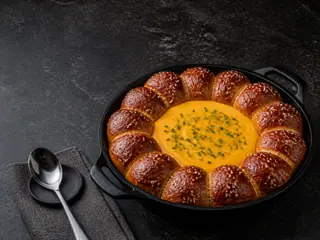 Coroa de pãezinhos de pretzel macios para destacar em volta de molho de cheddar e mostarda em uma frigideira de ferro fundido