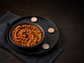 Tazón con mezcla de garbanzos especiados al horno dispuesta en una espiral continua junto a tres fichas sin marcas sobre la mesa