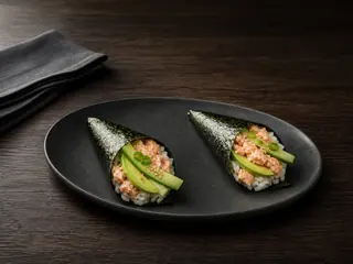 Two fully cooked salmon hand rolls arranged as a clean paired serving on a dark platter