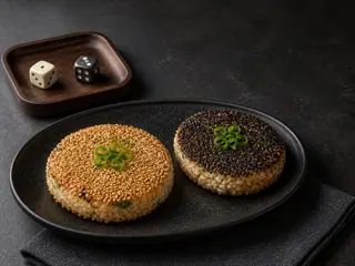 Two glossy sesame rice patties, one white-seeded and one black-seeded, arranged as a matched pair