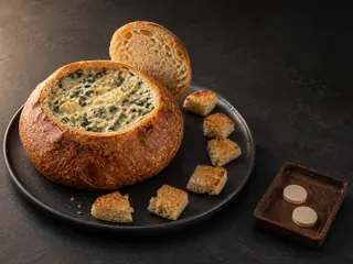 Round sourdough dip loaf with its cap propped open over hot spinach artichoke filling