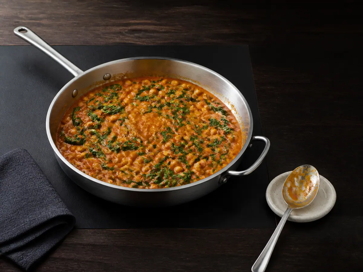Curry de grão-de-bico pronto, com espinafre verde murcho, em uma frigideira larga