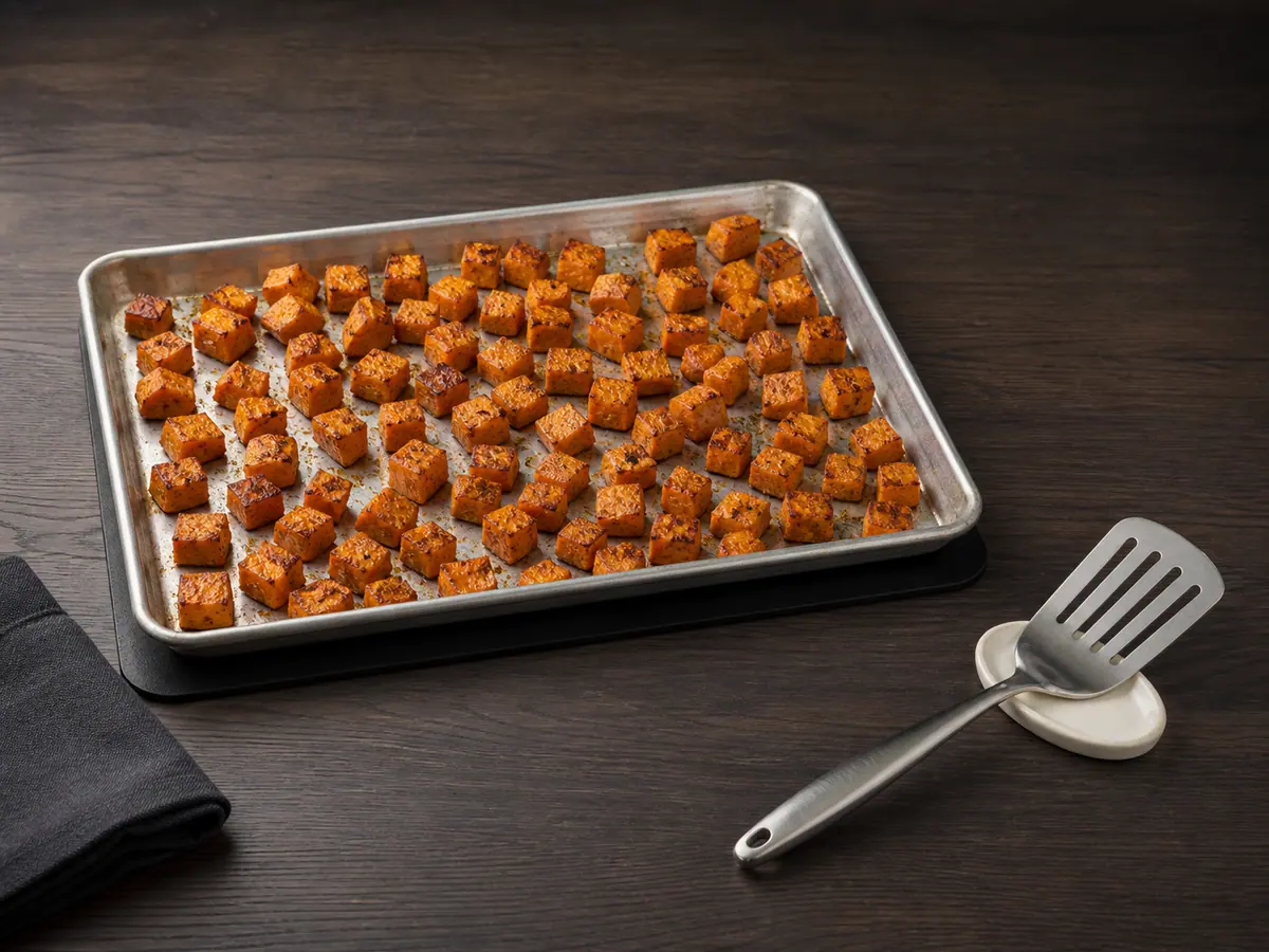 Cubos de batata-doce assada com bordas douradas em uma assadeira com borda
