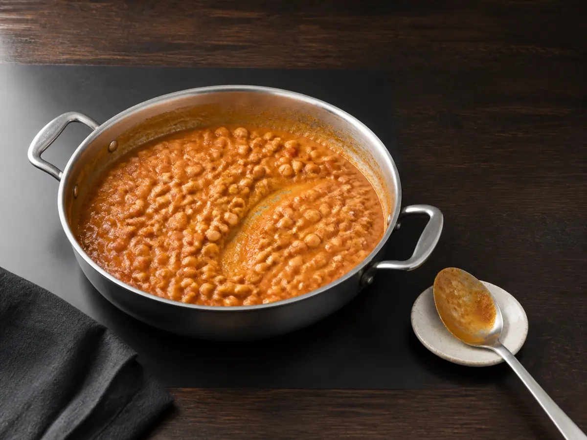 Curry espesso de grão-de-bico, tomate e coco cobrindo uma colher antes da adição do espinafre