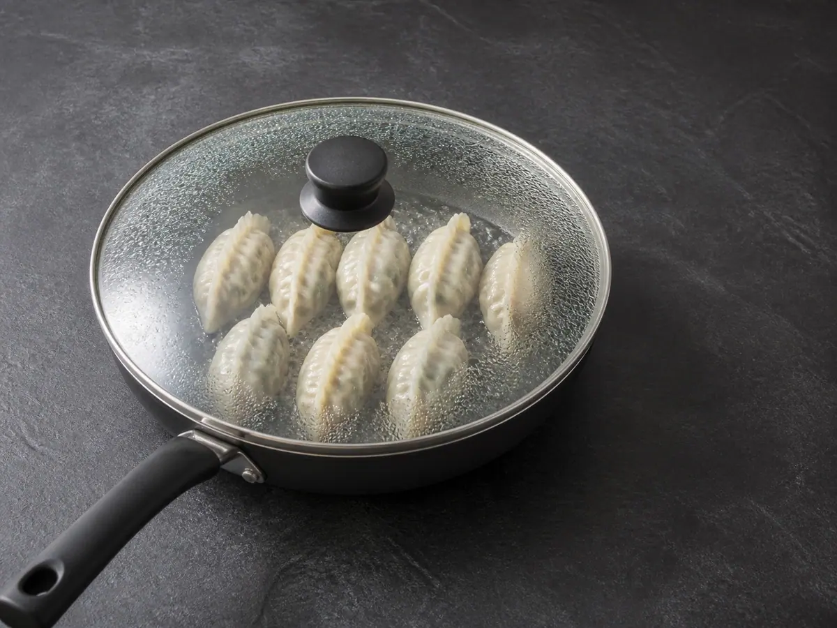 Eight dumplings steaming under a clear lid with tender slightly translucent wrappers